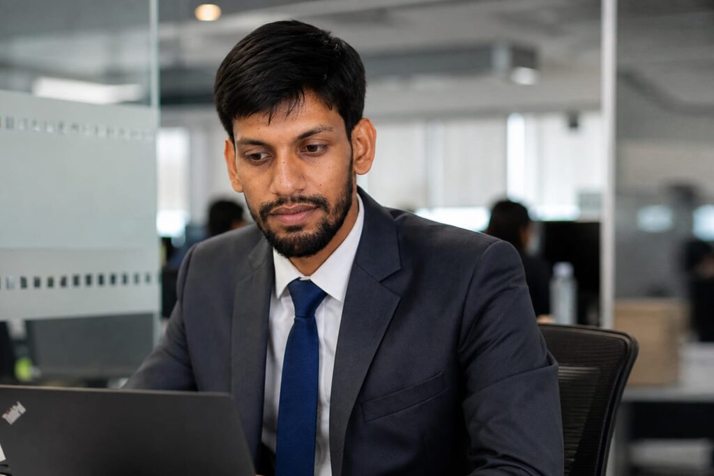 Kartick Shaw dressed in a professional suit, focused on his laptop while working in a modern office setting of Mahananda Consultancy